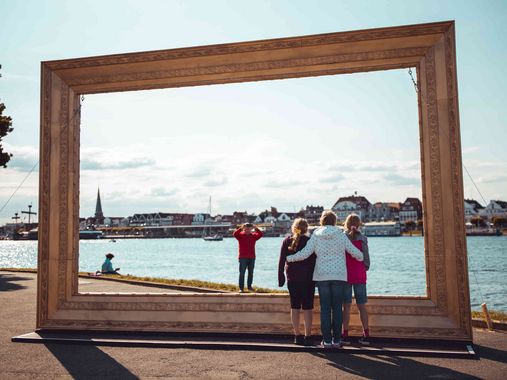 Familie macht ein Foto bei einem großen goldenen Bilderrahmen am Priwall